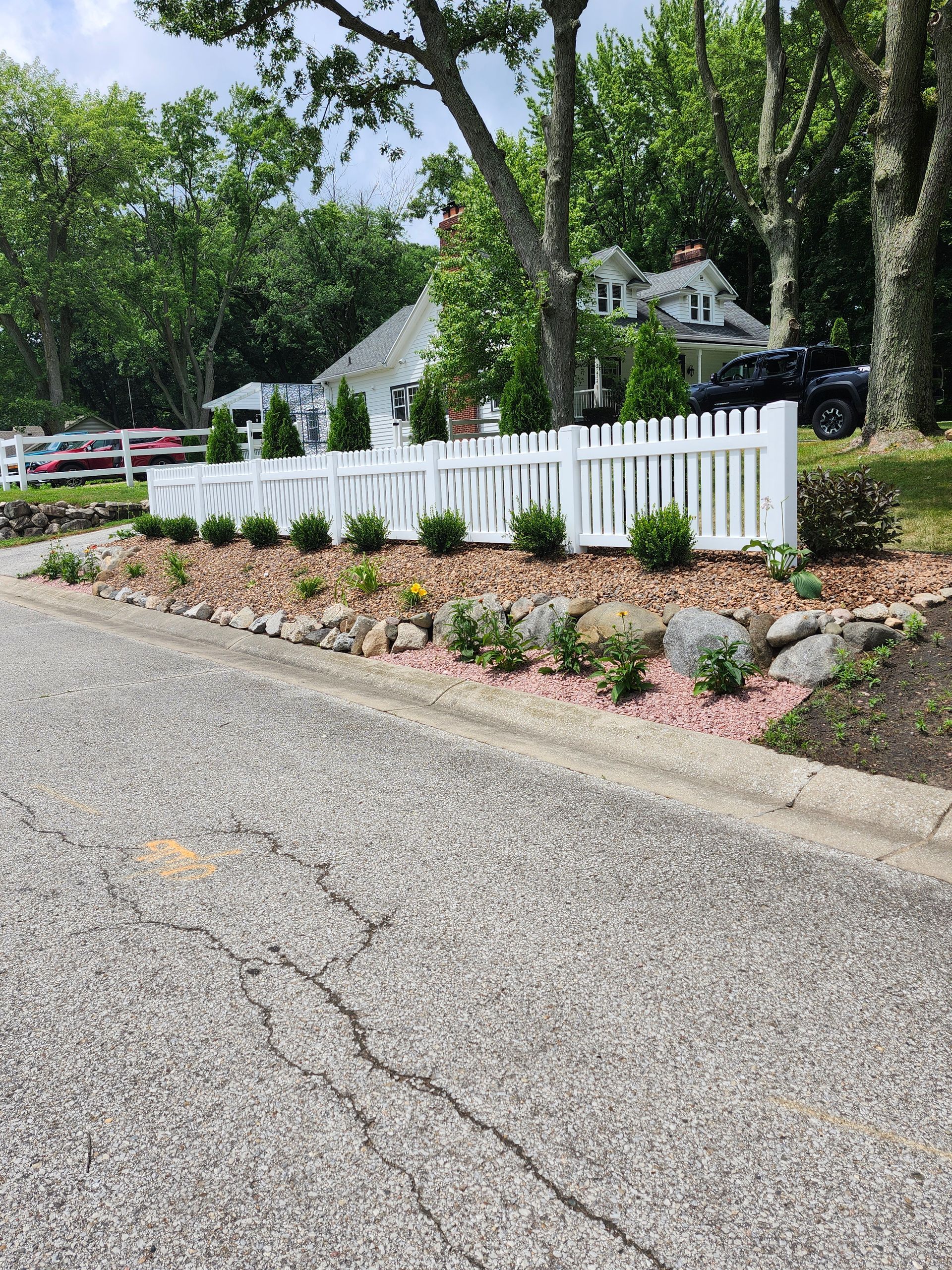 A white picket fence surrounds a gravel driveway in front of a house.