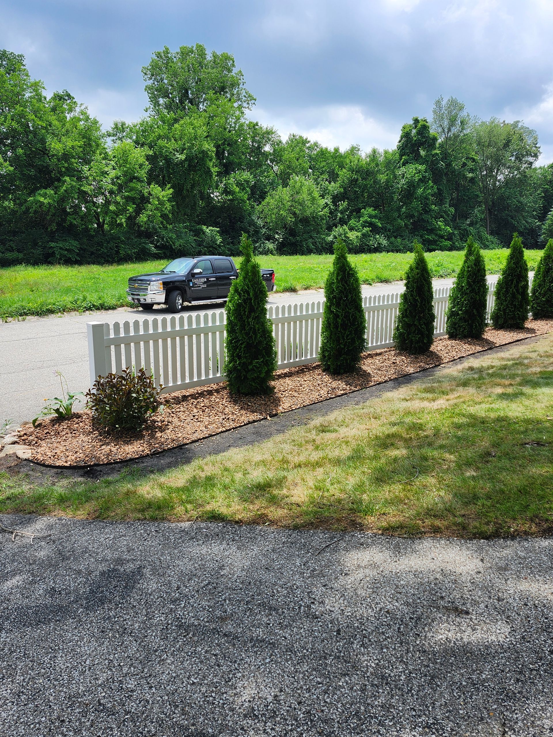 A car is parked in front of a white picket fence.