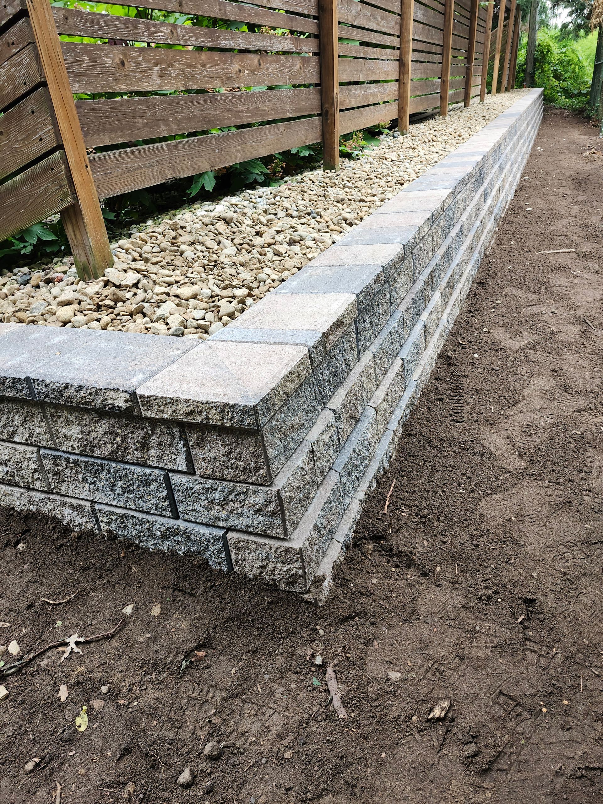 A stone wall is sitting in the dirt next to a wooden fence.