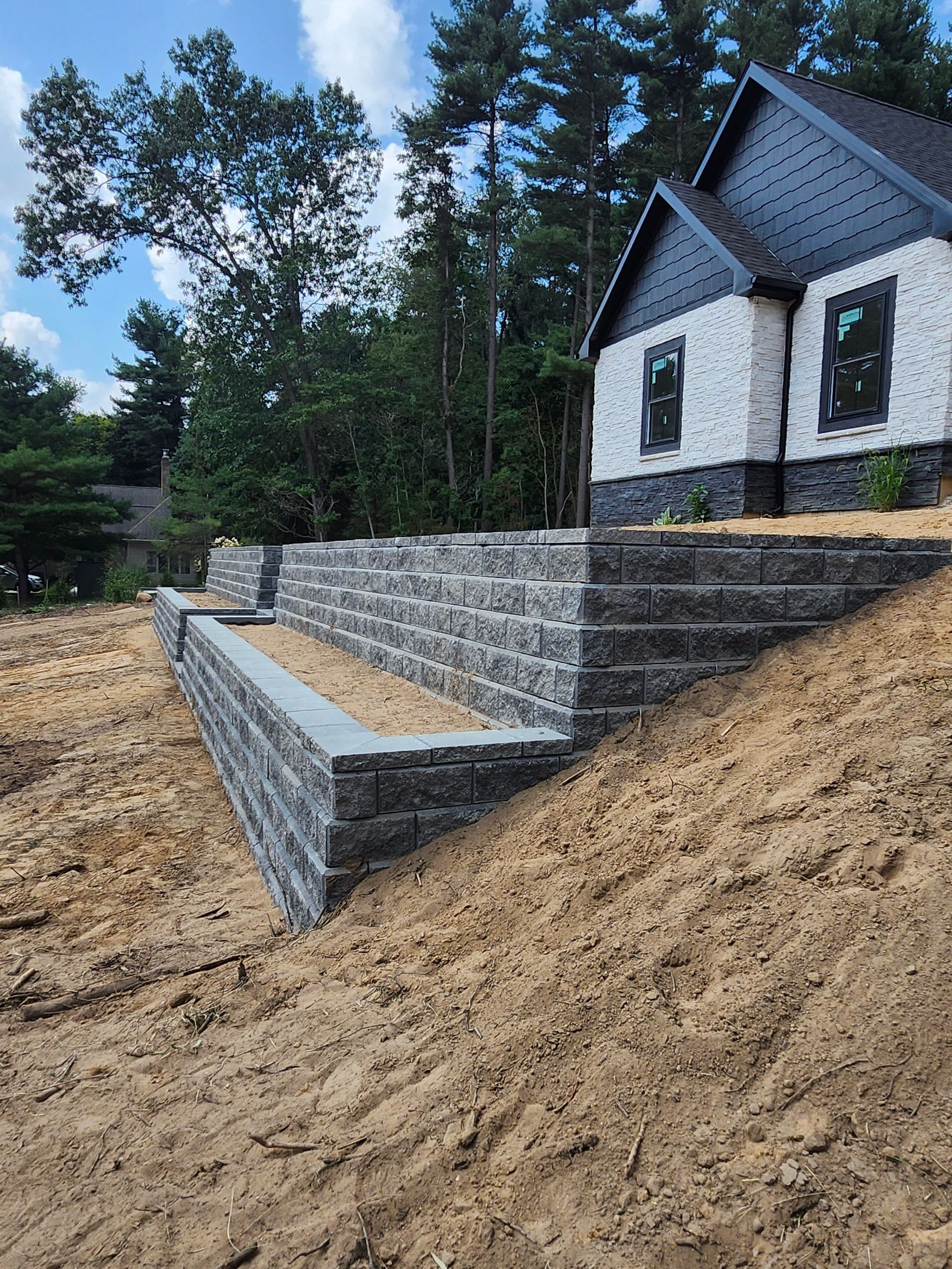 A house is sitting on top of a dirt hill next to a brick wall.