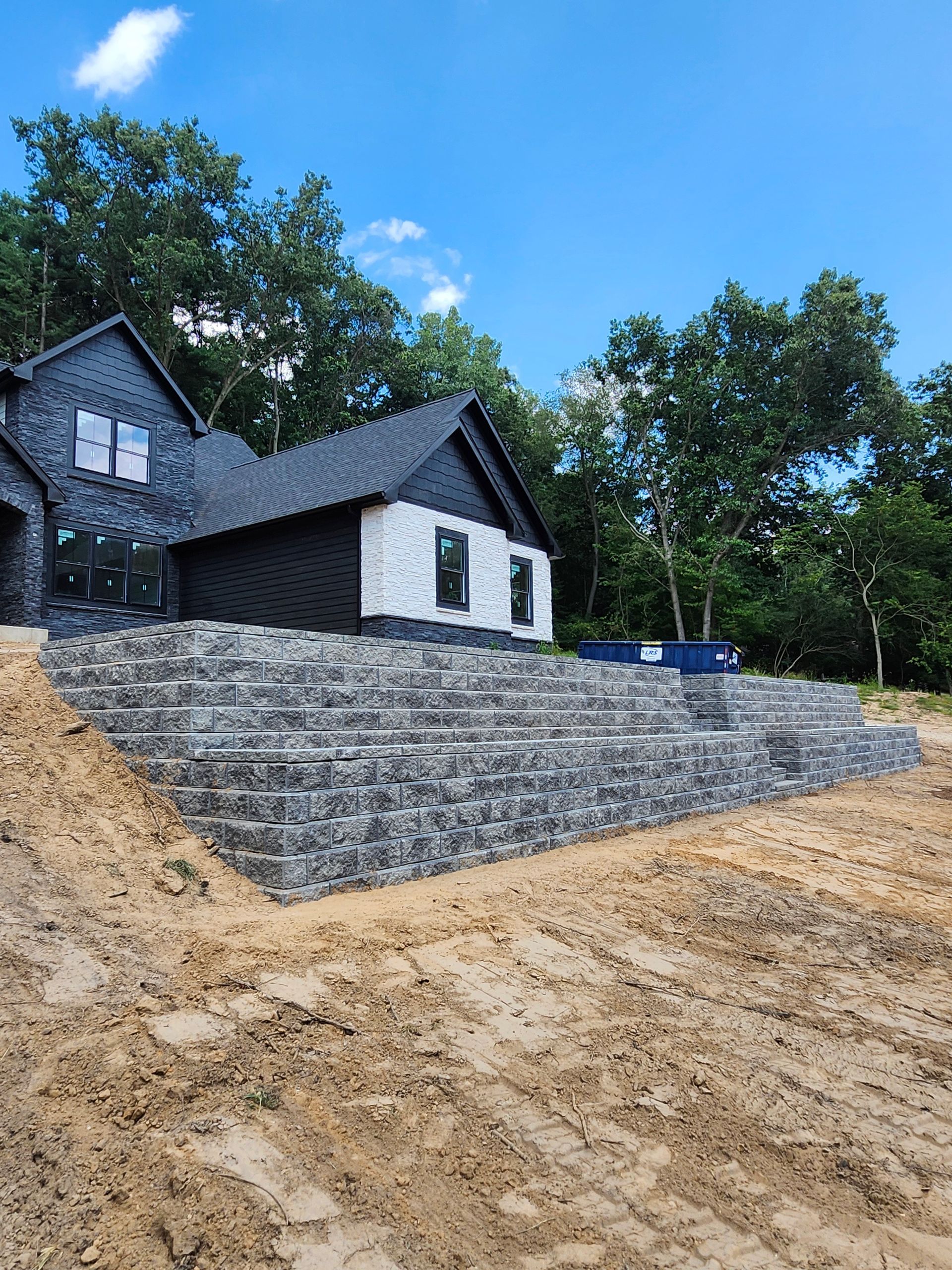 A house is sitting on top of a dirt hill next to a stone wall.