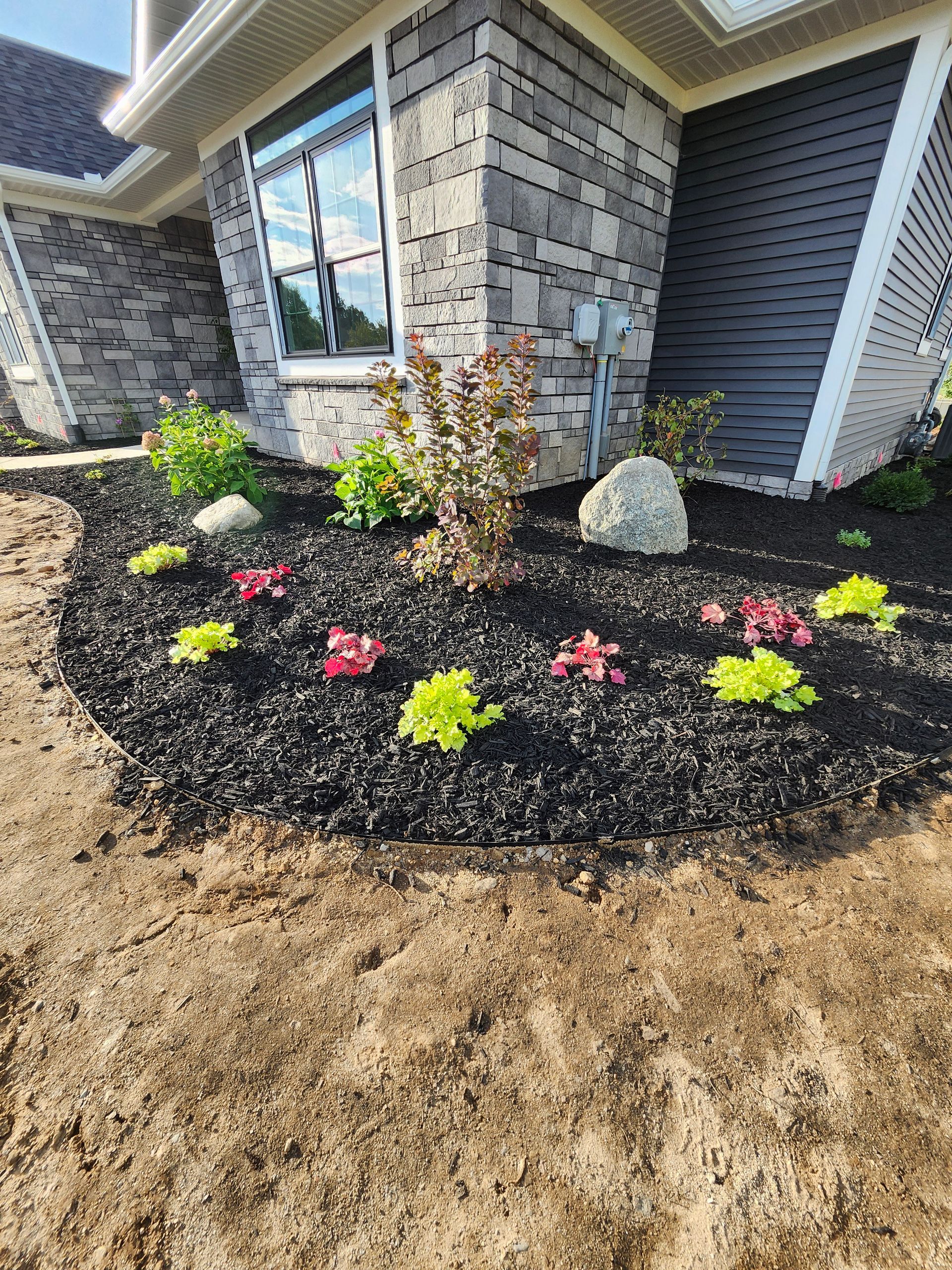 A lawn with flowers and rocks in front of a house.