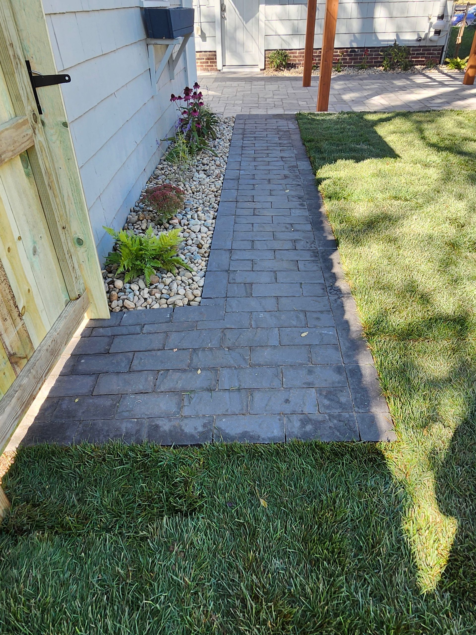A brick walkway leading to a house surrounded by grass and rocks.