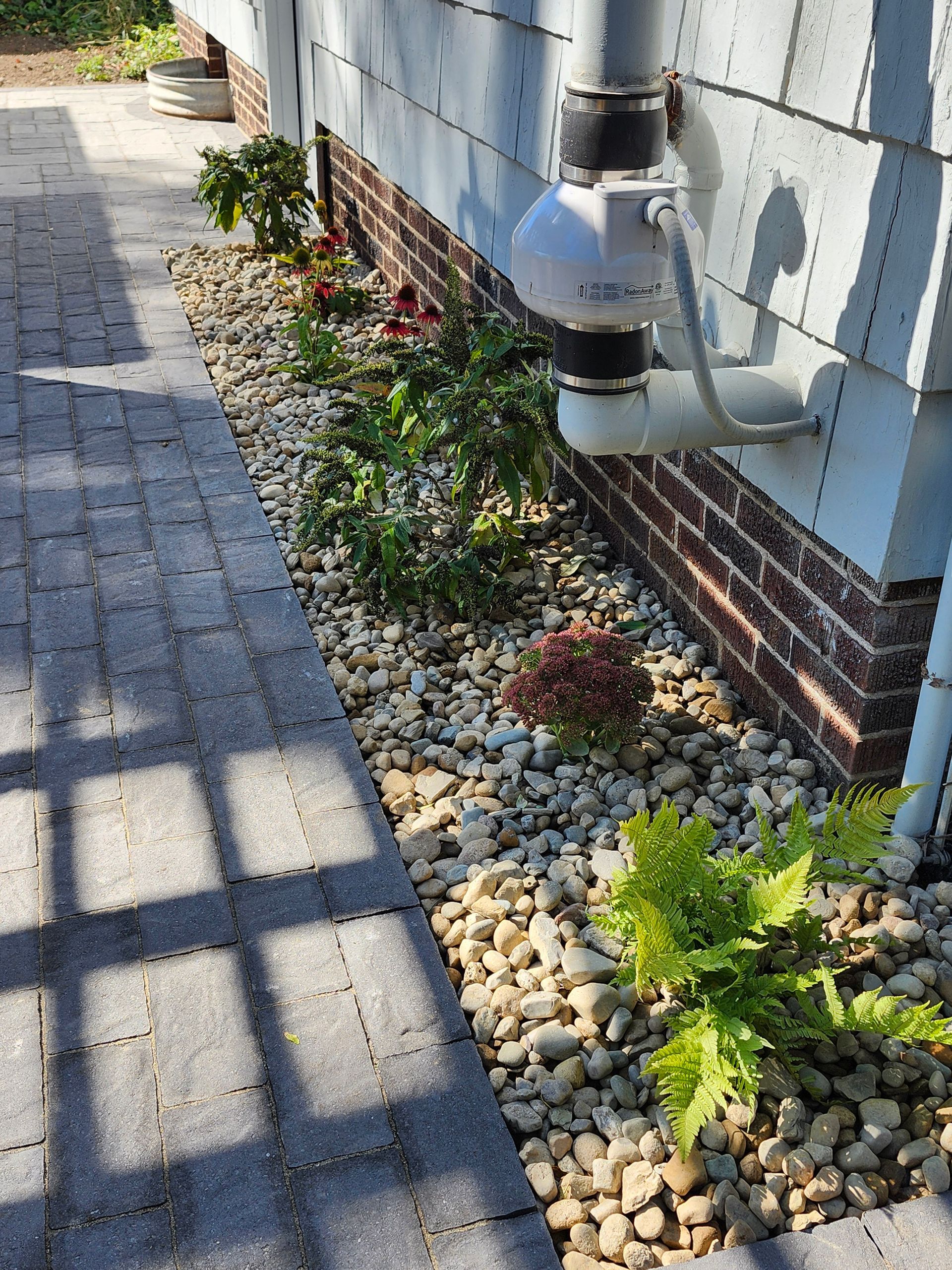 A brick walkway leading to a house with rocks and plants on the side.