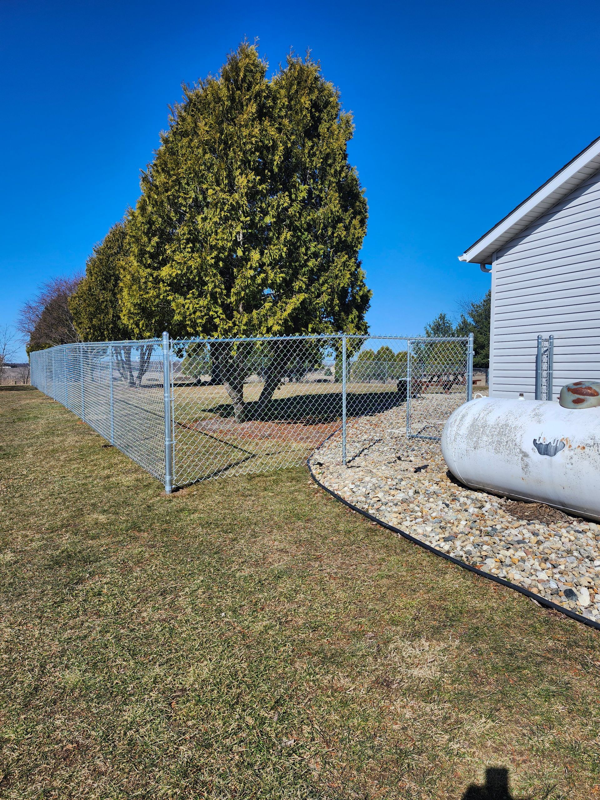 A chain link fence is surrounding a house and a propane tank.