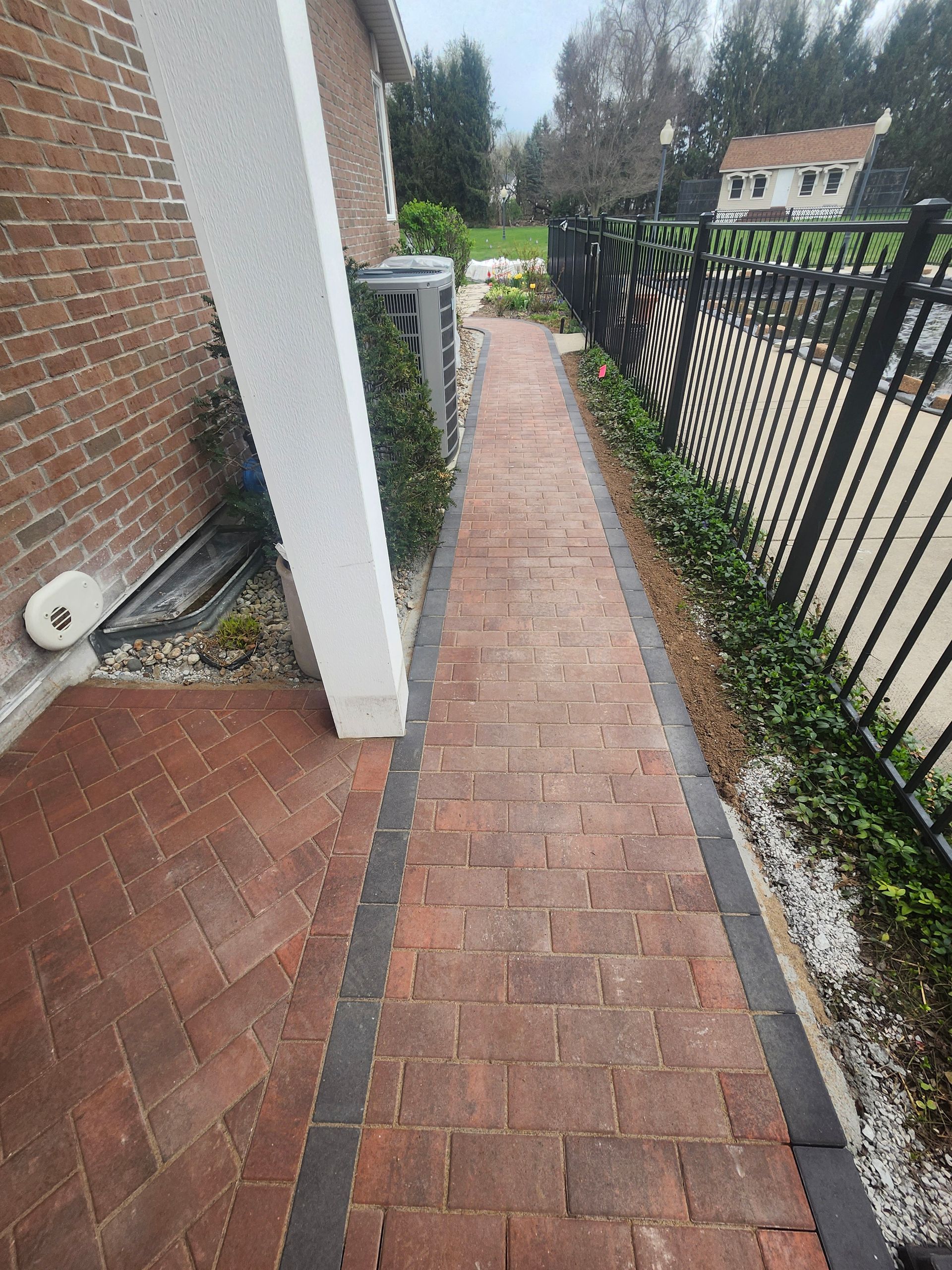 A brick walkway leading to a house next to a fence.