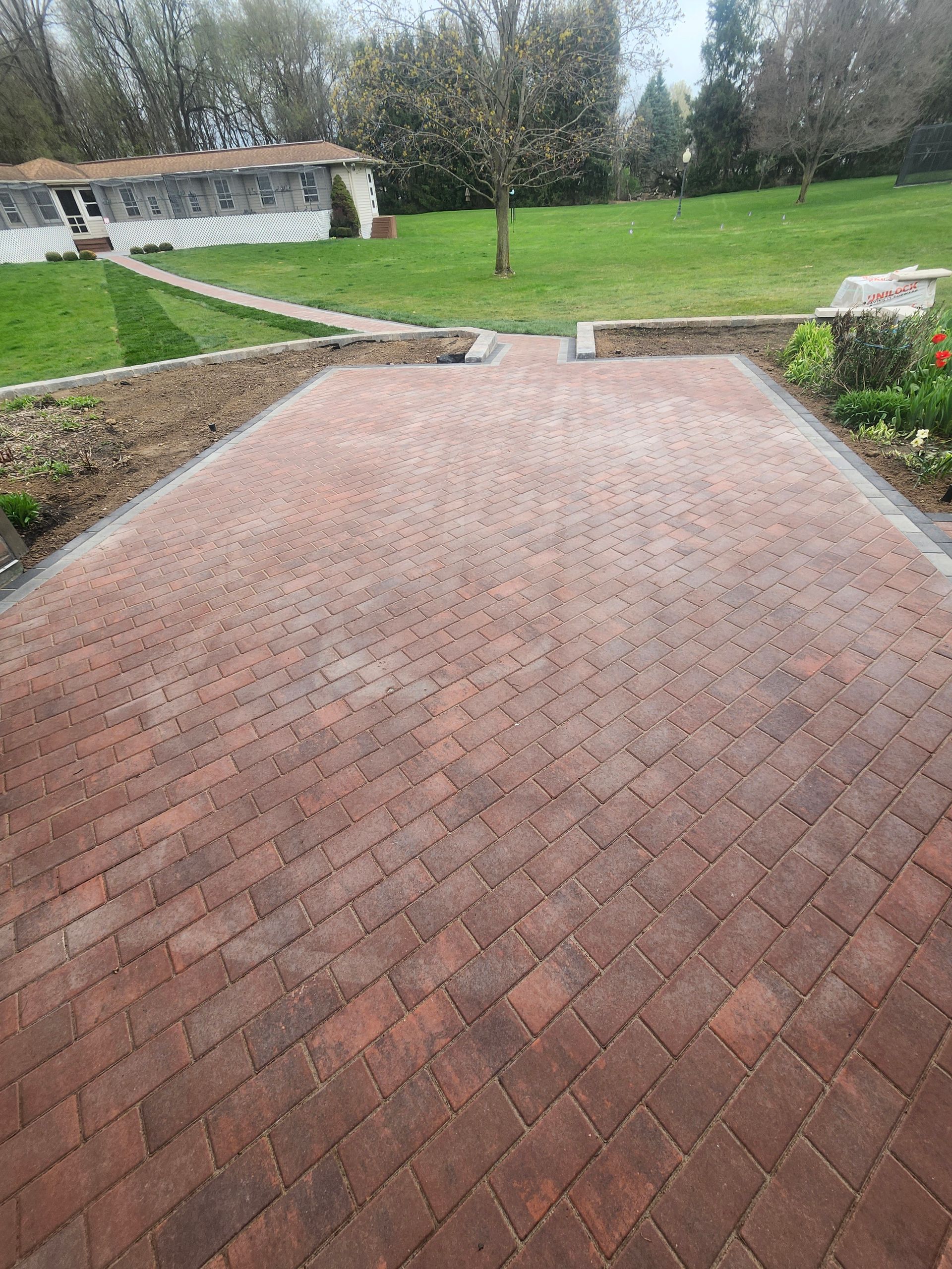 A brick driveway leading to a house with a lush green field in the background.