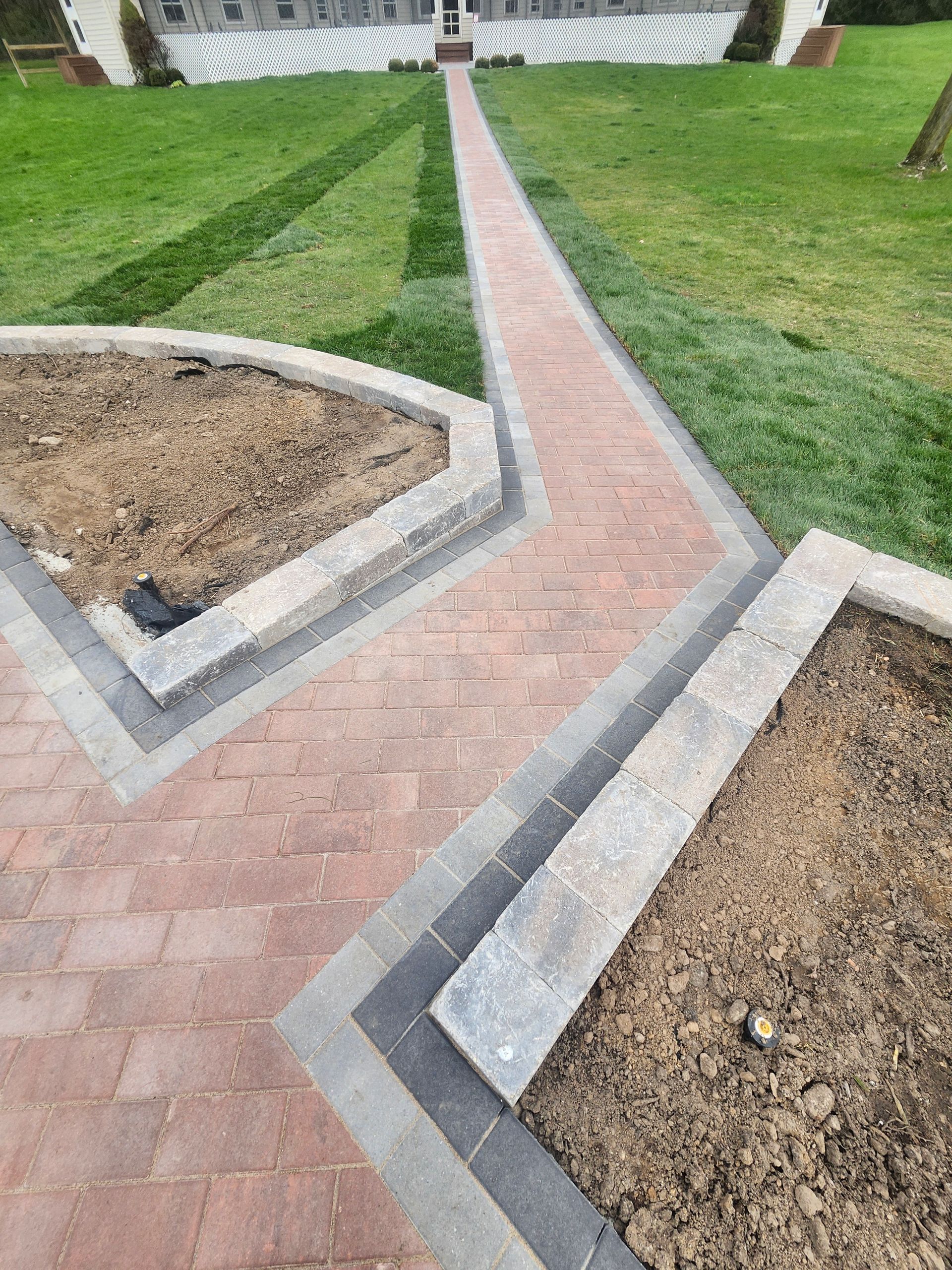 A brick walkway between two planters in a yard.