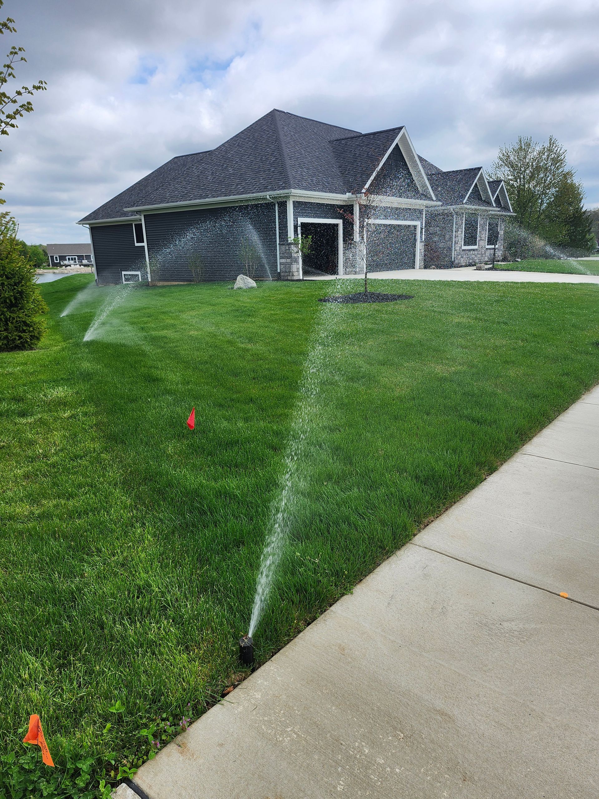 A lawn sprinkler is spraying water on a lush green lawn in front of a house.