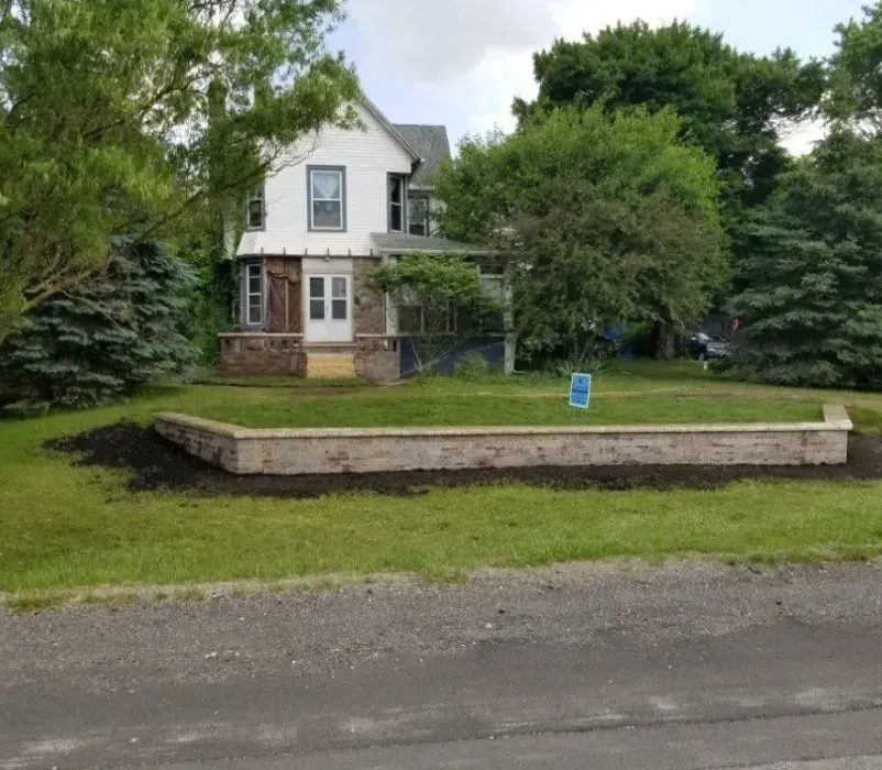 A white house with a brick wall in front of it.
