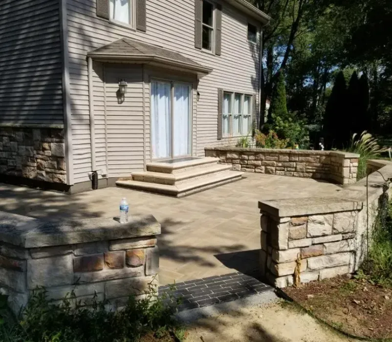 A house with a stone wall and a patio in front of it.