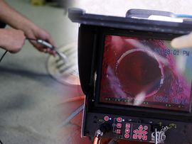 Hand holding a surgical instrument near a monitor showing a red endoscopic view in a medical setting