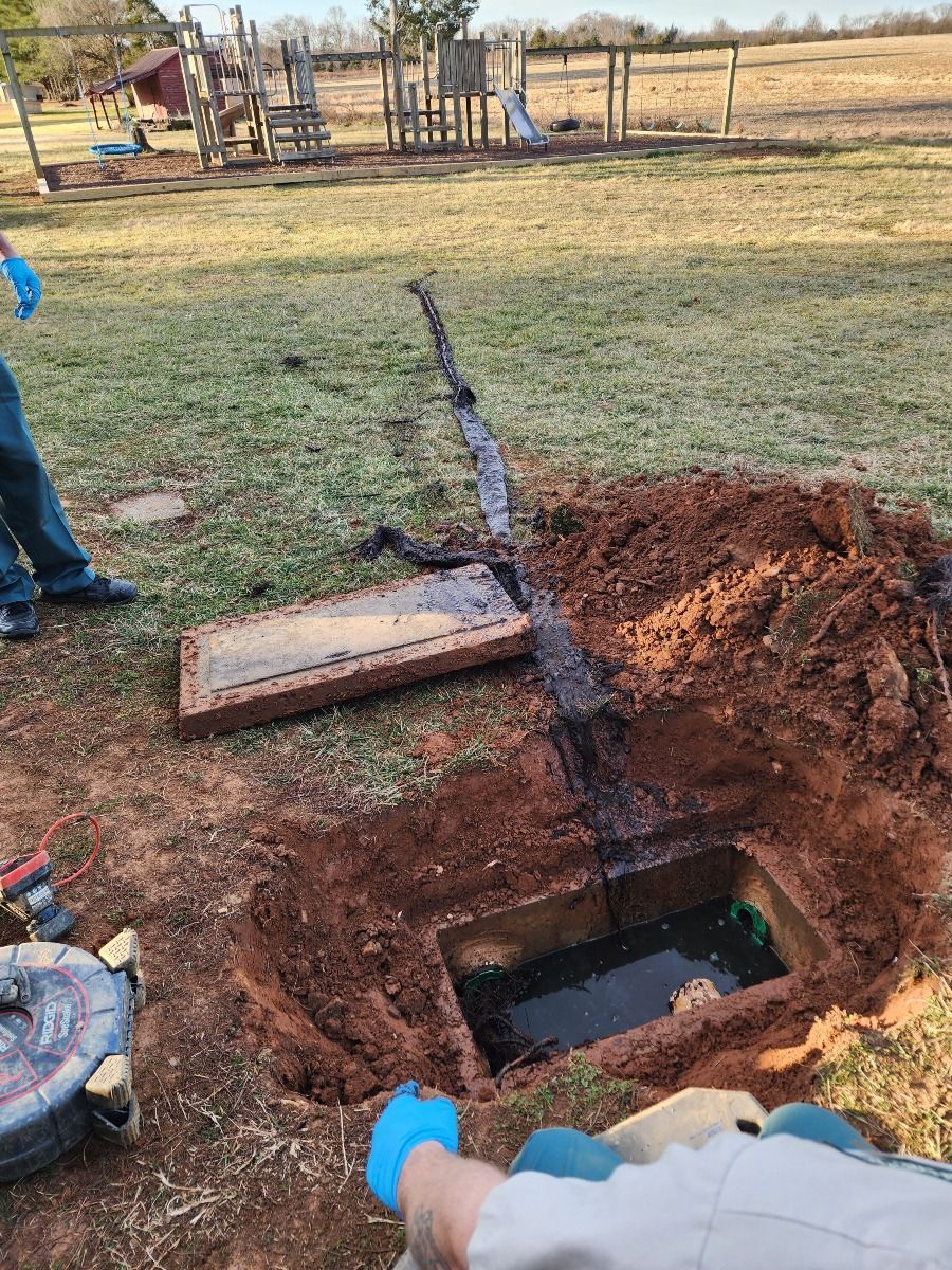 Open trench in a grassy yard with exposed utility pipe and workers nearby