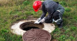 Worker in red hard hat cleaning a manhole opening outdoors
