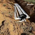 Underground utility conduit pipes laid in a dirt trench with a black cable junction box at the end