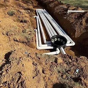 Underground utility conduit pipes laid in a dirt trench with a black cable junction box at the end