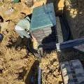 Worker installing a black utility box in a dirt trench outdoors