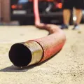 Red fire hose lying on pavement, with firefighters blurred in the background
