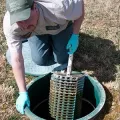 Worker in blue gloves lifting a metal filter from a round ground opening outdoors