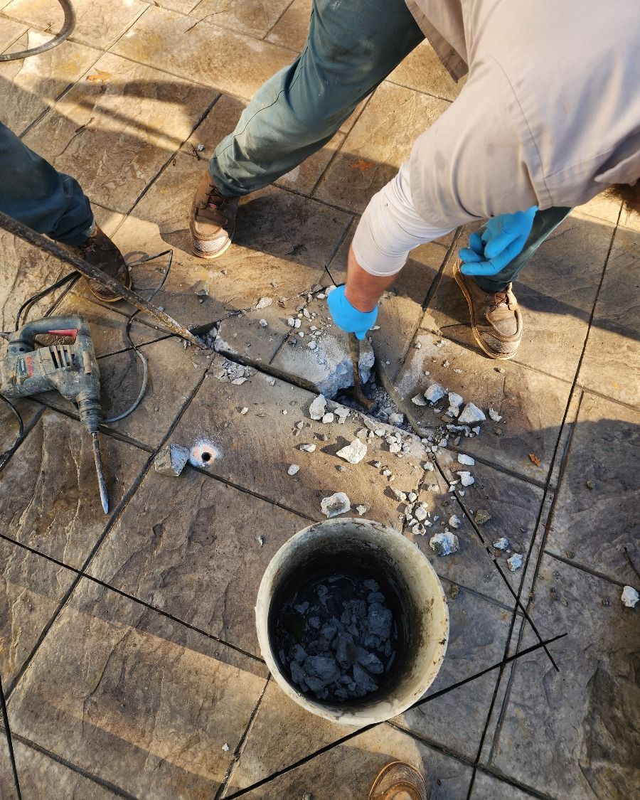 Workers in blue gloves breaking concrete around a round drain opening on a tiled floor