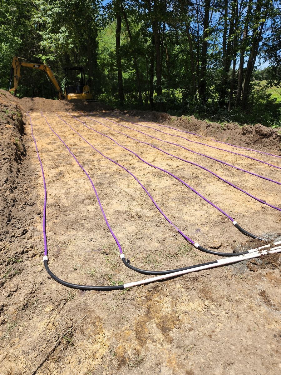 Freshly graded dirt lot with several purple irrigation lines laid across it beside a wooded area