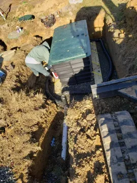 Worker stacking plastic crates beside a trench in a dirt yard