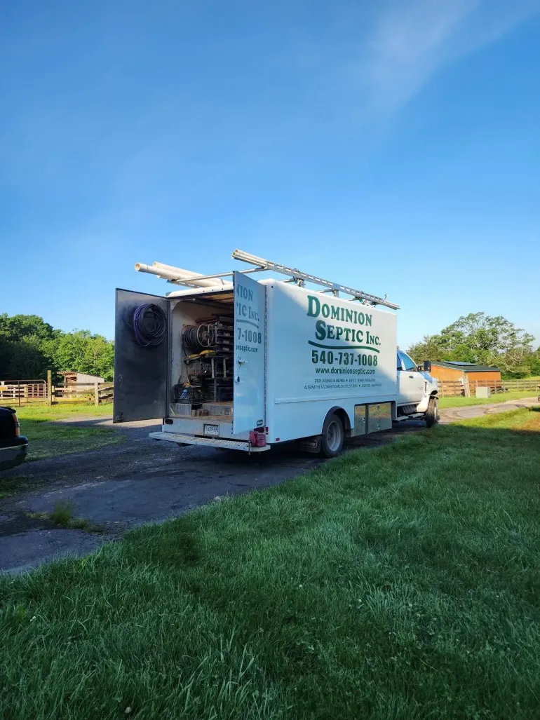 White moving truck parked on a grassy roadside under a blue sky, rear door open.