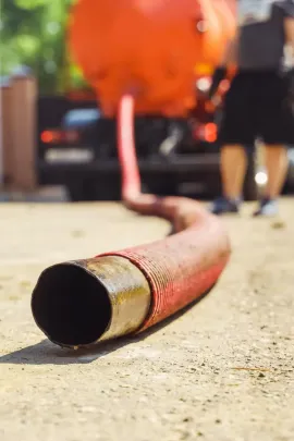Charred fire hose lying on pavement, with blurred orange fire truck and firefighters in the background