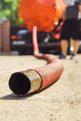 Charred fire hose lying on pavement, with blurred orange fire truck and firefighters in the background