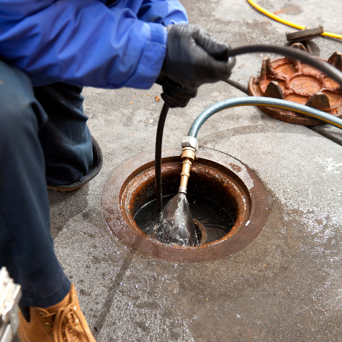 A man is cleaning a manhole cover with a hose.