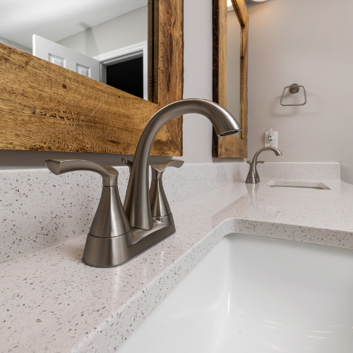 A bathroom sink with two faucets and a mirror