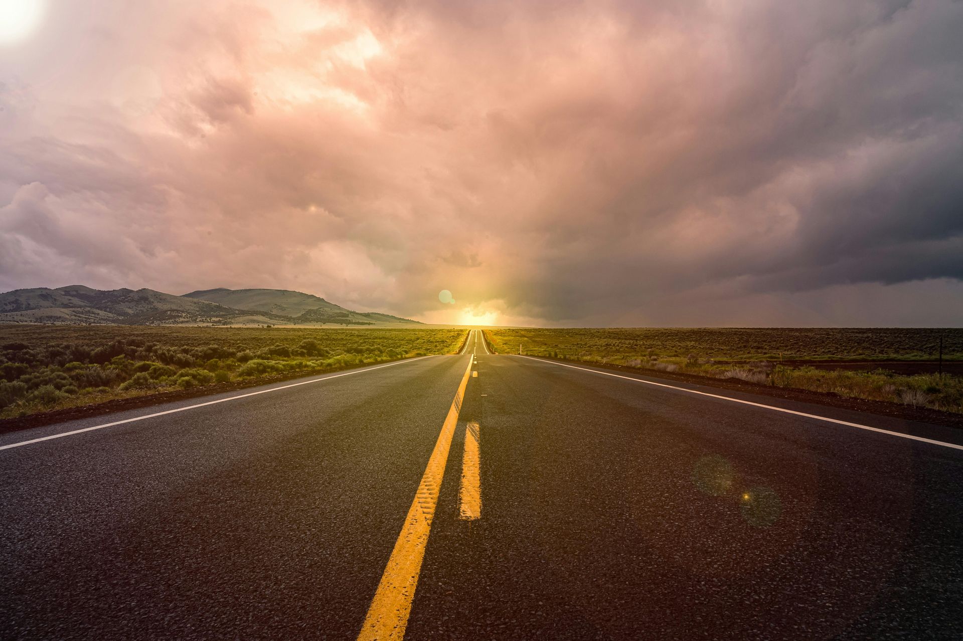A road with a sunset in the background and the sun shining through the clouds.