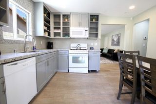 Gray kitchen with white appliances, glass-door cabinets, and dining table leading to living room.