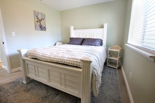 White bed in a light green bedroom with a window. A grey rug and artwork are present.