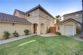 Beige two-story house with a garage and green lawn under a clear sky.