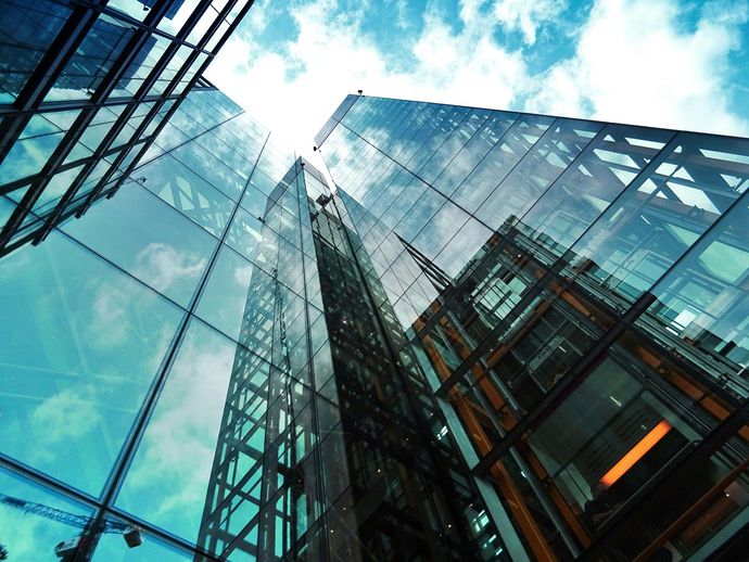 Glass skyscrapers against a blue sky with clouds, viewed from below.