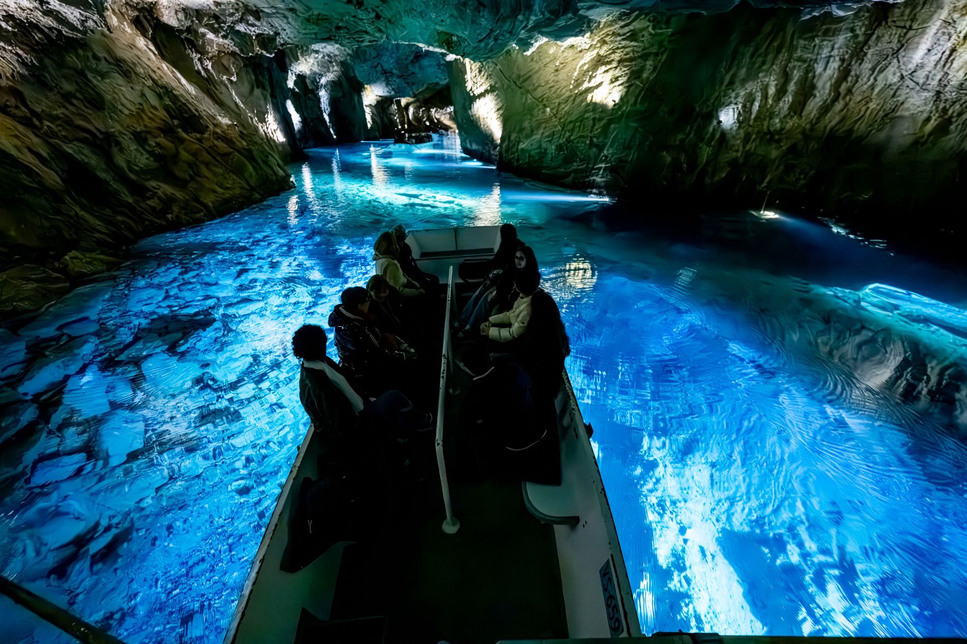Dark boat on glowing blue underground river inside a cave with rock walls and waterfalls