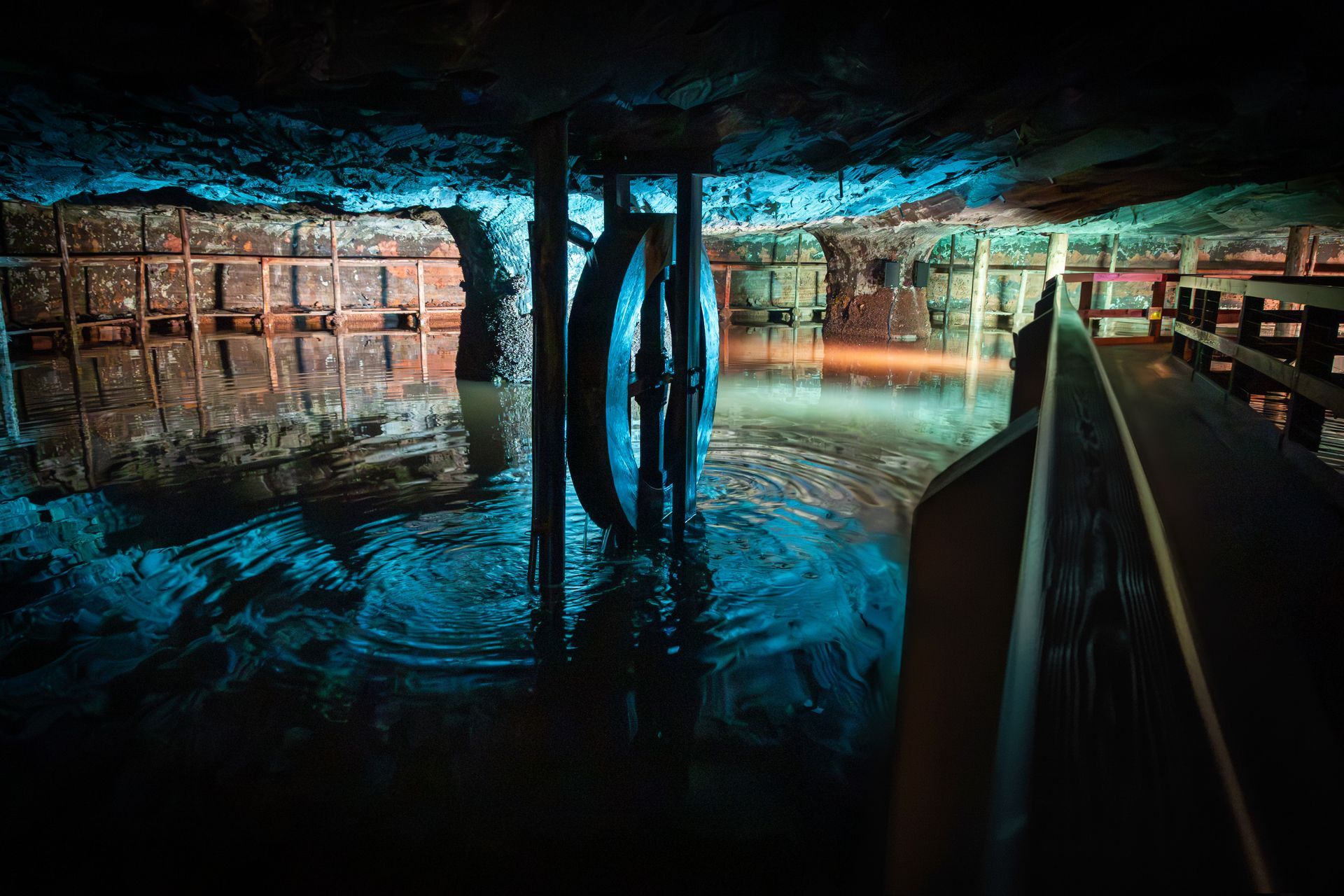 Dim underground chamber with blue-lit water, central columns, and a walkway along the right side
