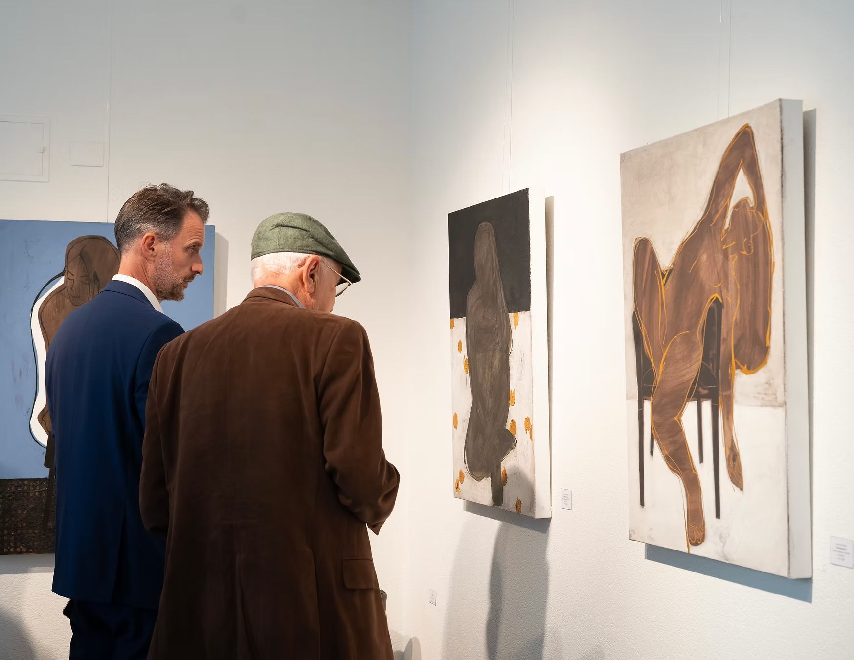 Two people viewing abstract paintings in a bright gallery