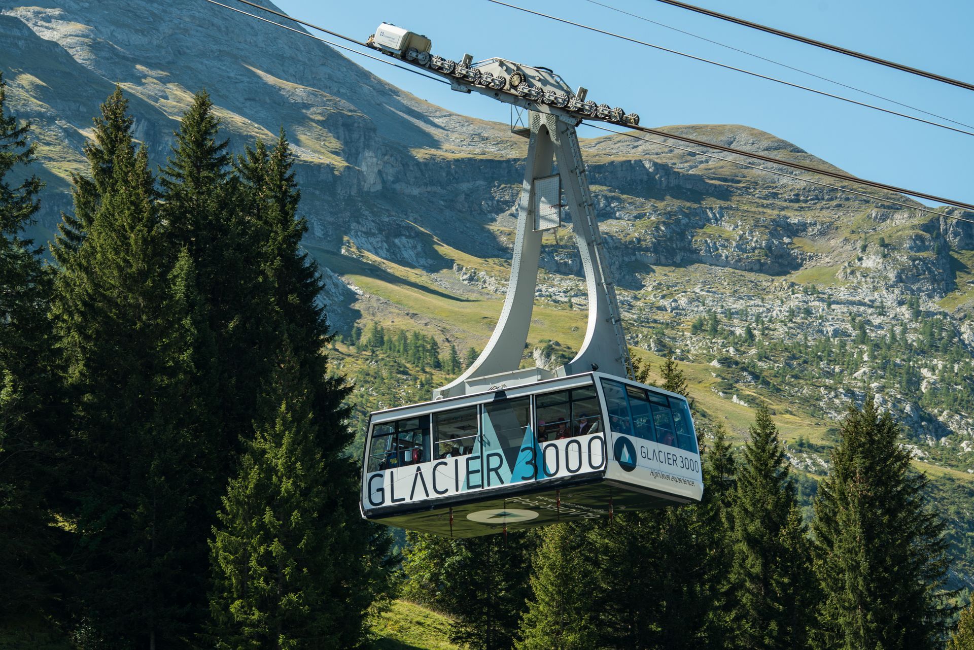 Schneebedeckter Berggipfel mit einem modernen Gebäude und einer Seilbahn unter klarem, hellem Himmel.