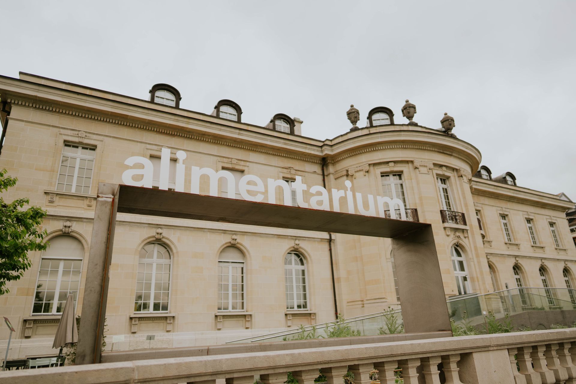Historic beige building with “alimentarium” sign and arched windows under an overcast sky