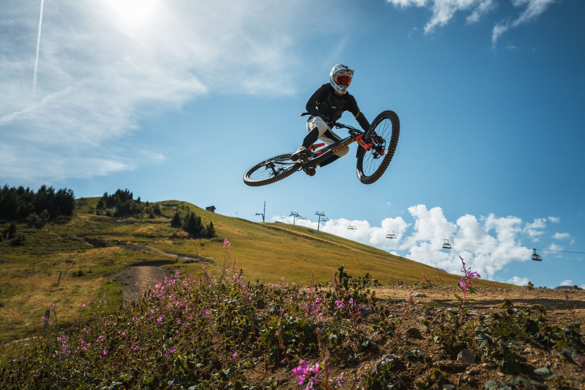 Ein Mountainbiker fährt einen grasbewachsenen Hügel hinunter, im Hintergrund sind die Berge unter blauem Himmel zu sehen.