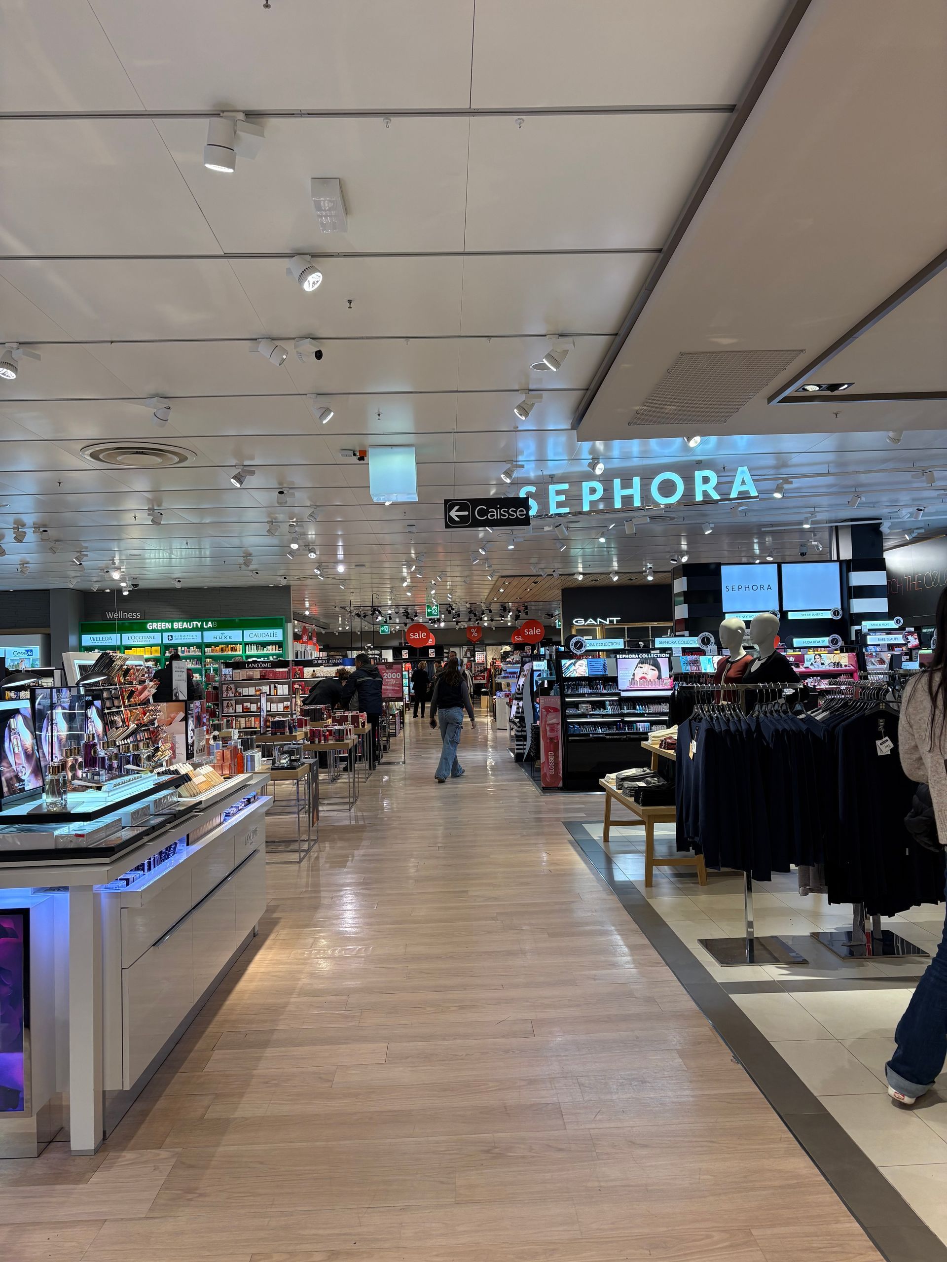Busy shopping mall aisle with a Sephora store ahead and shoppers browsing displays
