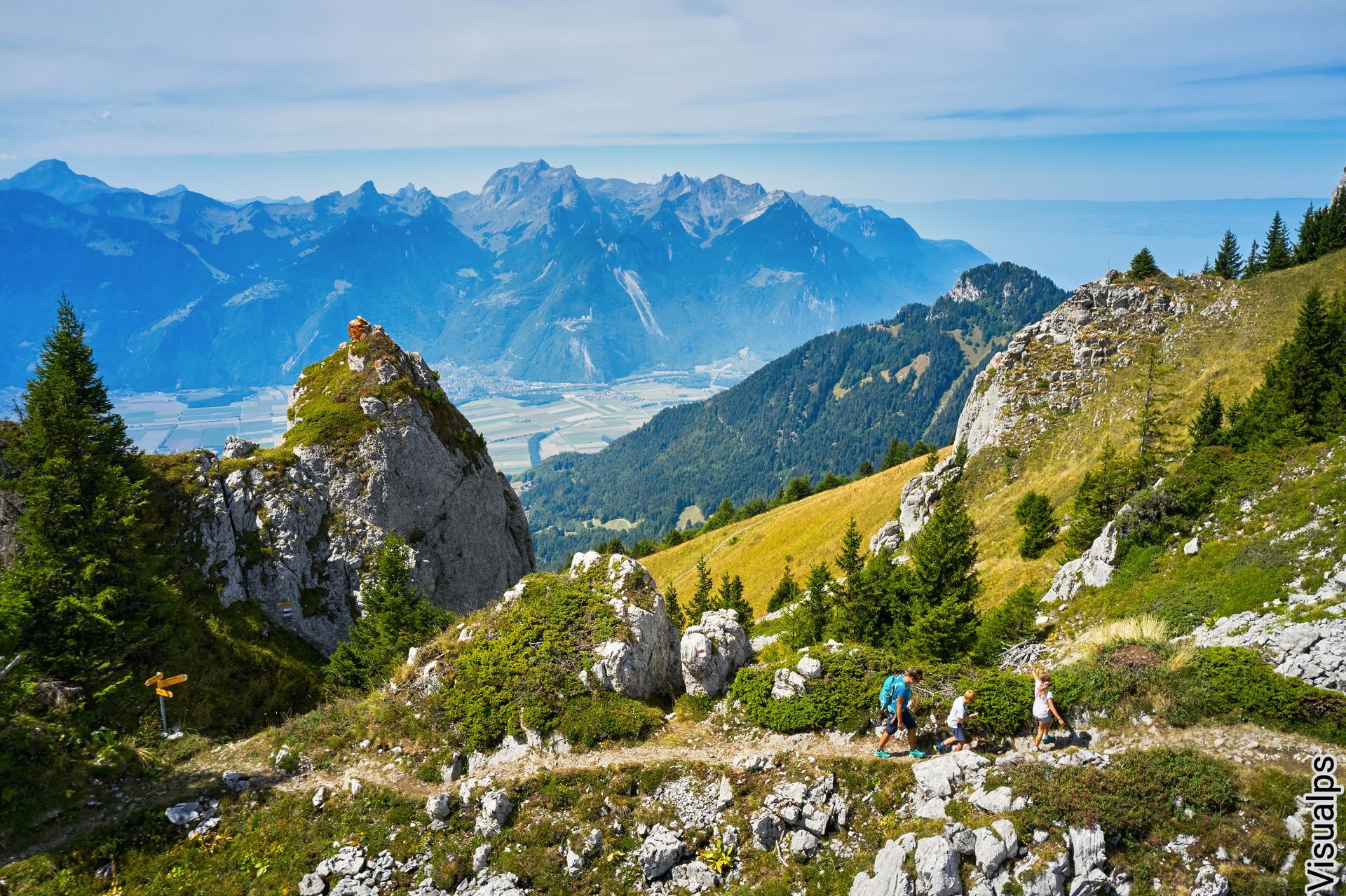 Schneebedeckter Berggipfel mit einem Gebäude und Skifahrern vor dem Hintergrund schneebedeckter Gipfel unter strahlend blauem Himmel.