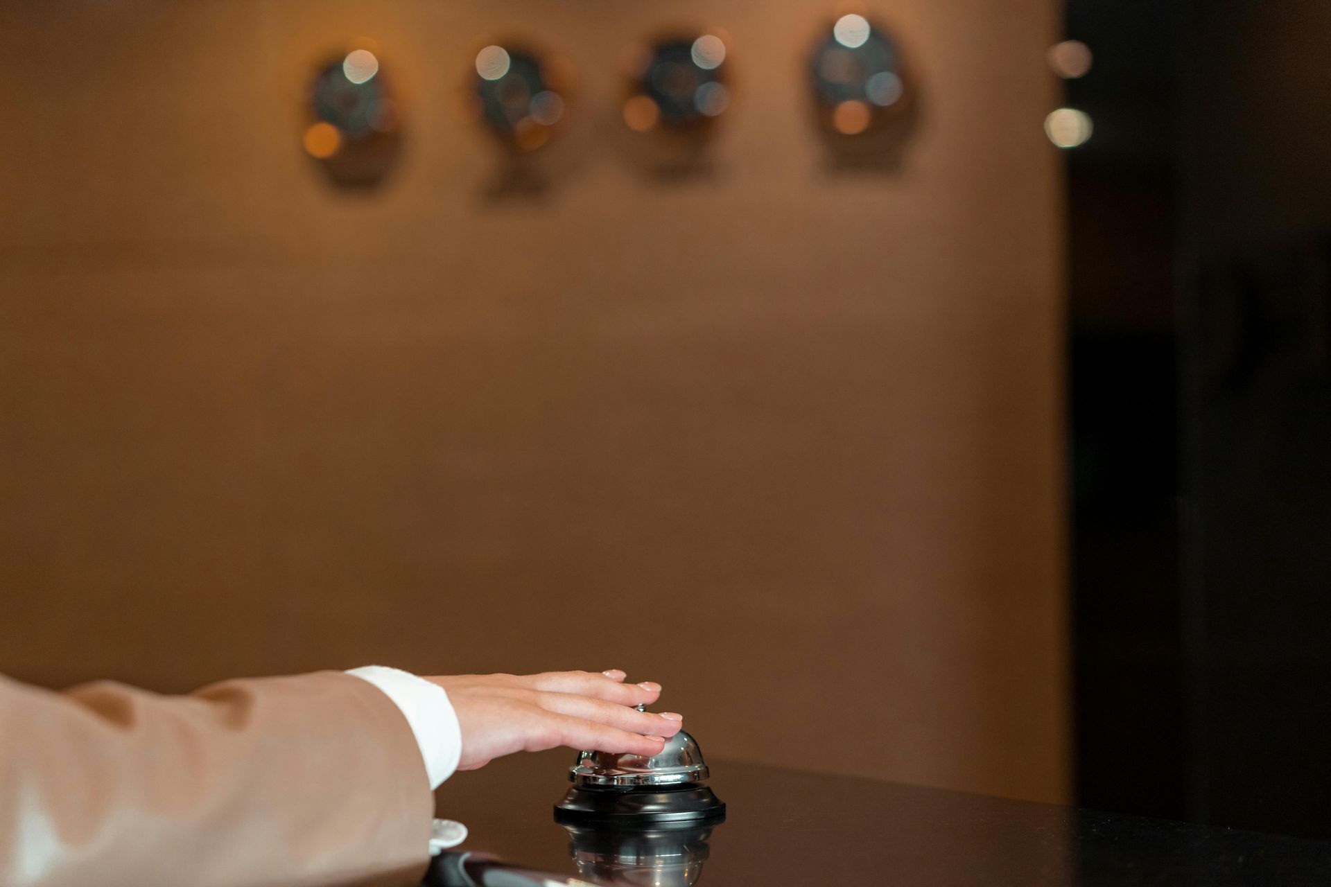 Hand pressing a service bell on a counter in a warm-lit room