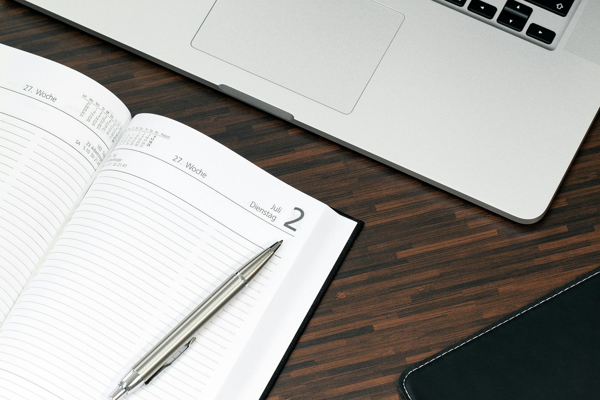 Un agenda ouvert avec un stylo, un ordinateur portable et un tapis de souris sur un bureau en bois.