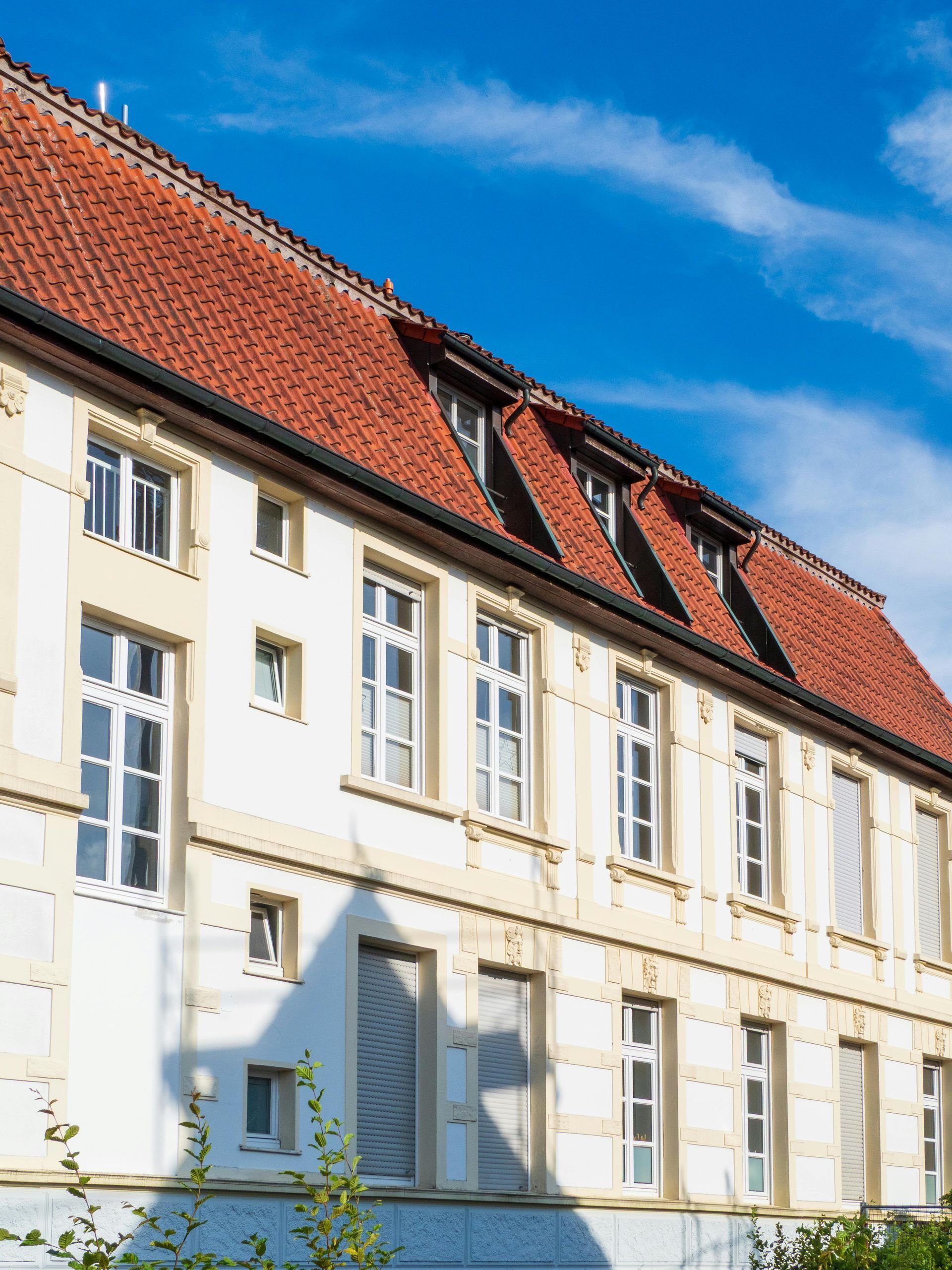 Weißes Gebäude mit rotem Ziegeldach und Dachgauben unter blauem Himmel