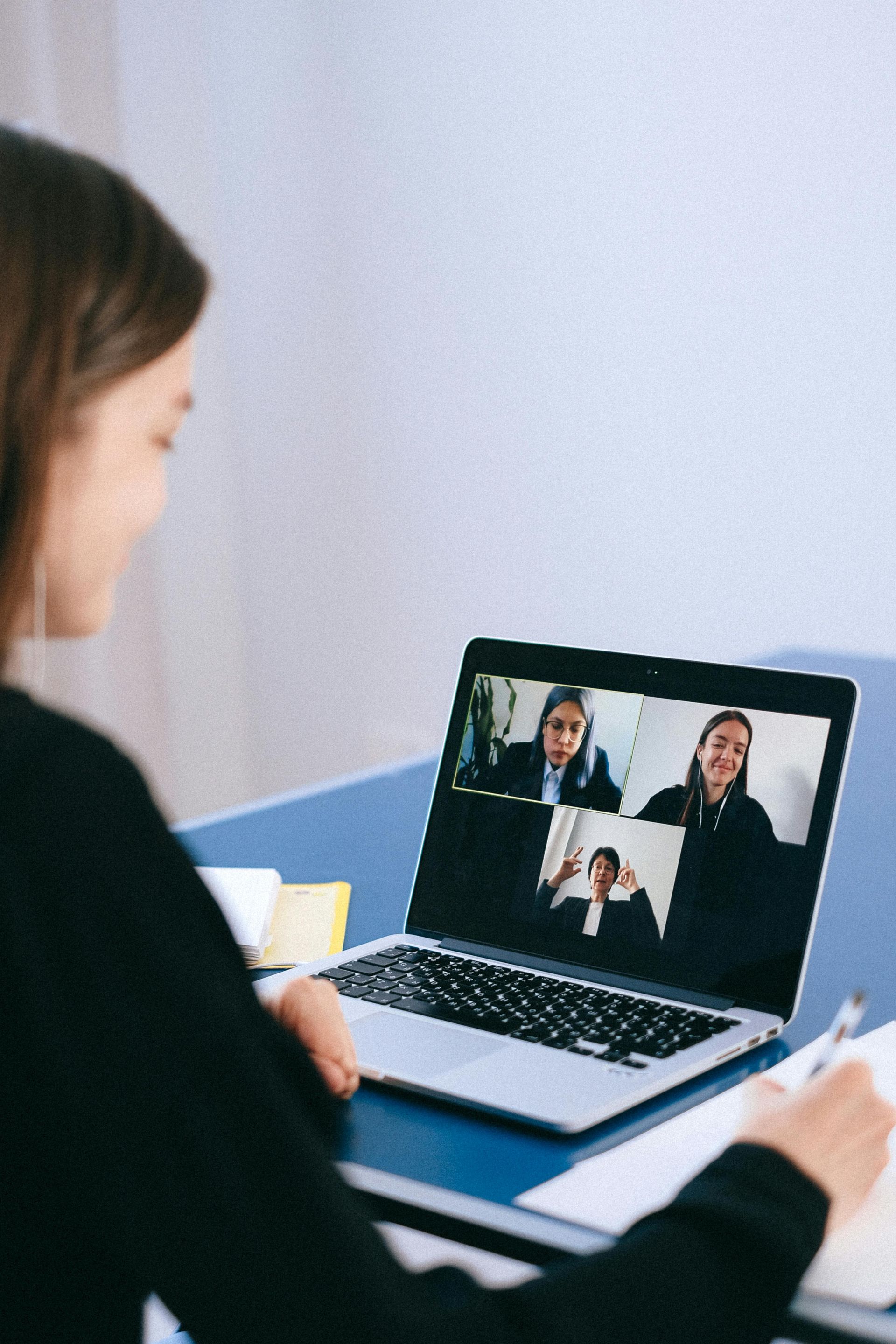 Eine Person arbeitet während eines Videoanrufs mit drei Teilnehmern auf dem Bildschirm an einem Laptop.