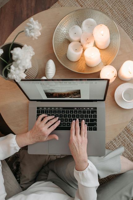 Hände, die auf einem Laptop neben einem runden Tisch mit brennenden Kerzen und Blumen tippen.