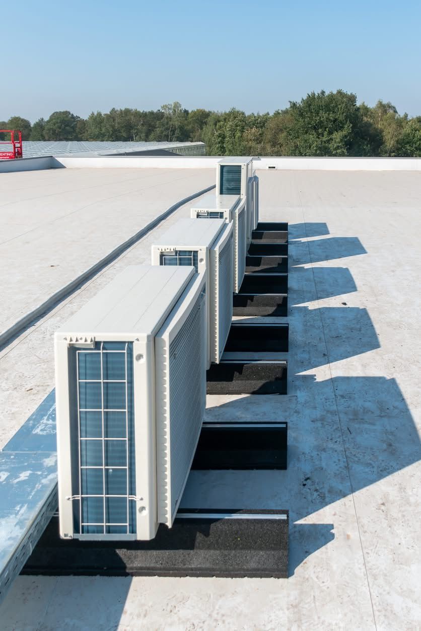 An outdoor central air conditioning unit sits on a concrete pad surrounded by gravel against the side of a house.